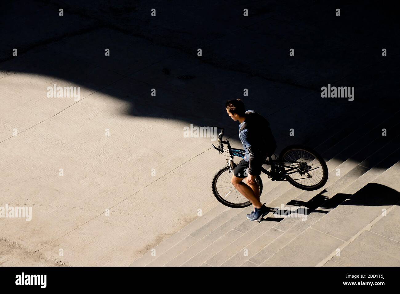 Belgrado, Serbia - 18 marzo 2020: Giovane uomo che porta una bicicletta giù per le scale della città in una giornata di sole, vista ad angolo alto da dietro Foto Stock
