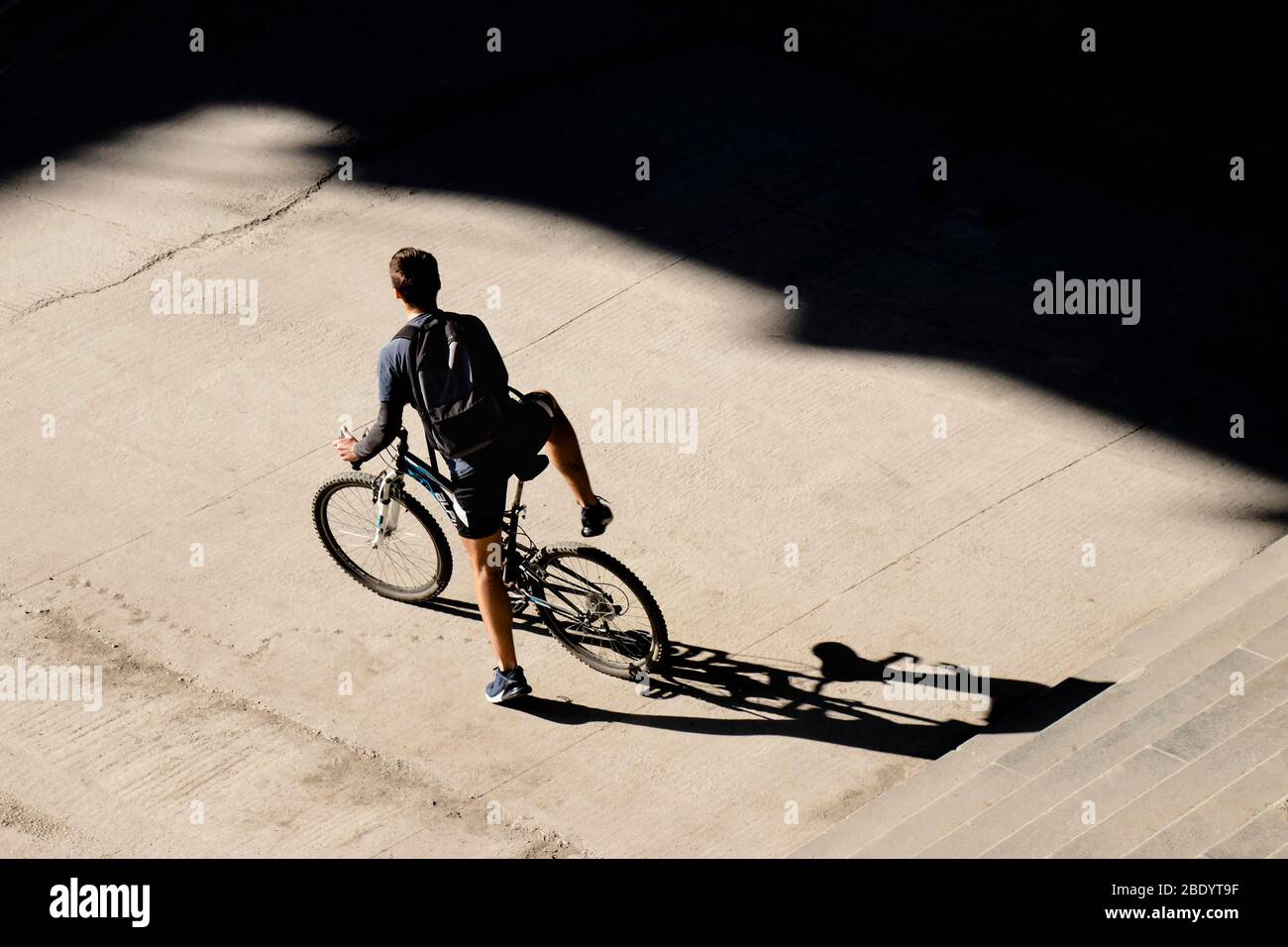 Belgrado, Serbia - 18 marzo 2020: Giovane uomo che si porta in bicicletta sul marciapiede della strada della città di fronte alle scale pubbliche in una giornata di sole, alta angolo di retrvi Foto Stock
