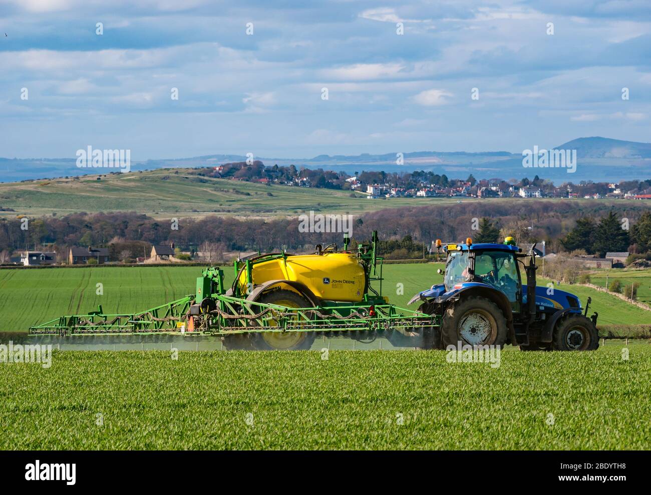 Campo di irrorazione dei trattori in paesaggio arabile con vista di Firth of Forth, East Lothian, Scozia, Regno Unito Foto Stock