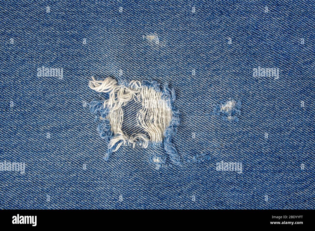 primo piano del foro sfilacciato in tessuto blu denim Foto Stock