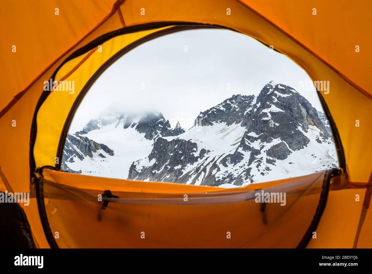 Guardando fuori da un grande rifugio tenda cupola giallo ad un massiccio picco roccioso avvolto dalle nuvole nelle montagne Talkeetna dell'Alaska. Foto Stock