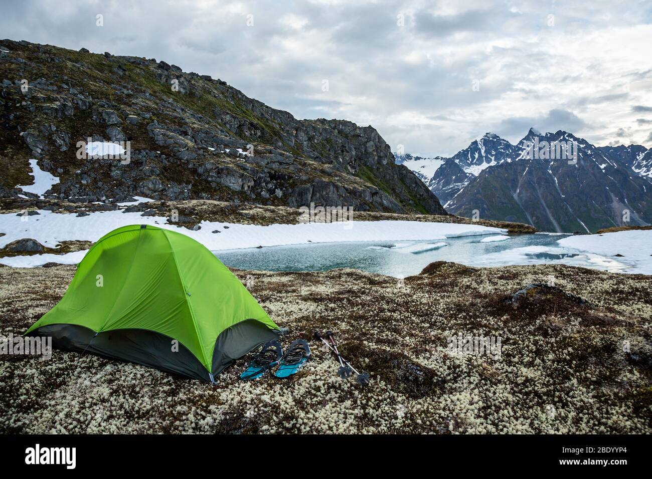 Tenda verde per una persona con racchette da neve su un lago parzialmente ghiacciato. Campeggio solo in primavera nella remota natura selvaggia dell'Alaska. Foto Stock