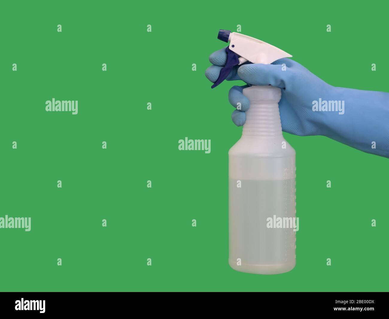 Una mano che indossa un guanto in gomma blu può contenere un flacone di plastica riempito con soluzione detergente da una vista laterale, appoggiato su una superficie verde solida. Foto Stock
