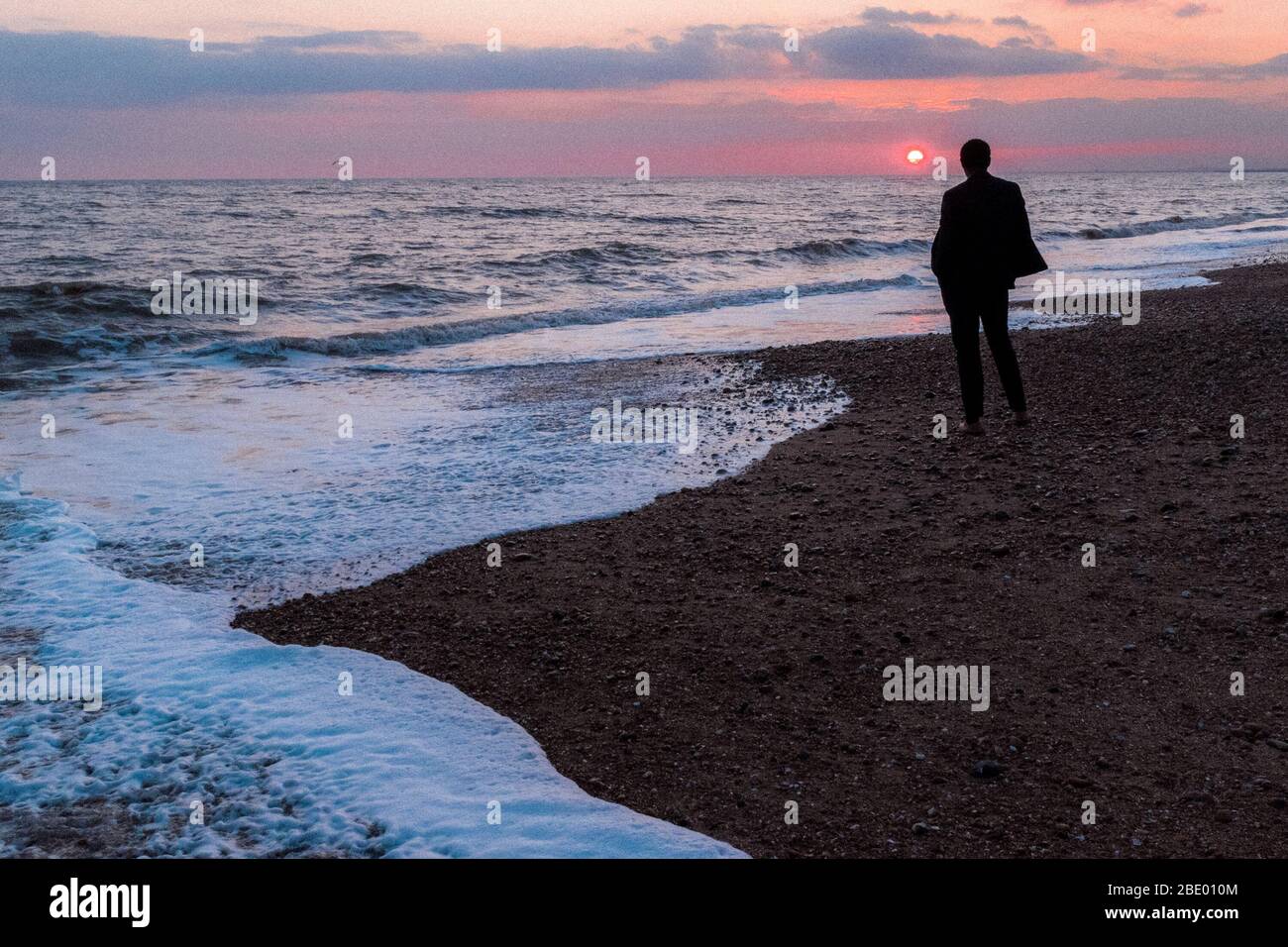 Un uomo che si accerce al tramonto mentre la marea entra intorno a lui, Brighton Beach, Brighton & Hove, Inghilterra Foto Stock
