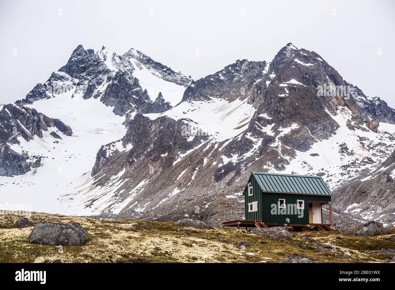 Un piccolo edificio verde nella natura selvaggia dell'Alaska offre rifugio agli sciatori e agli escursionisti del Talkeetna Mountain Range. Foto Stock