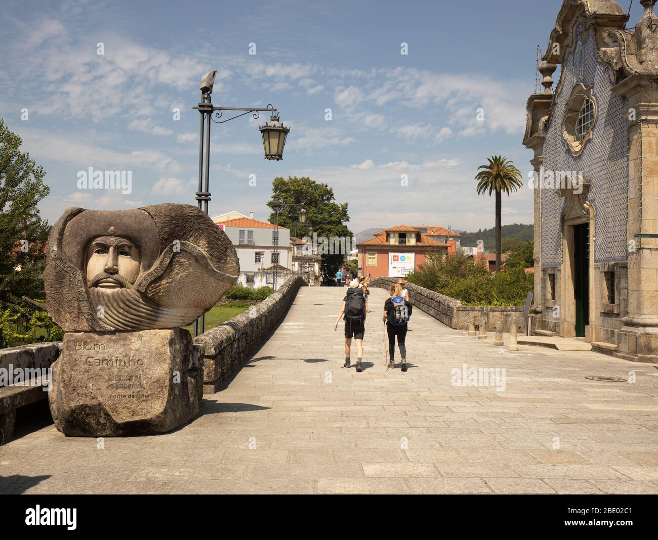 Due escursionisti femminili sul percorso centrale di Camino Portugués passeggiando davanti a una grande statua di benvenuto Bom Camino a Ponte de Lima nel Portogallo del Nord Foto Stock