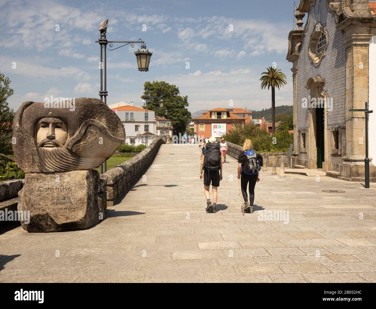 Due escursionisti femminili sul percorso centrale di Camino Portugués passeggiando davanti a una grande statua di benvenuto Bom Camino a Ponte de Lima nel Portogallo del Nord Foto Stock