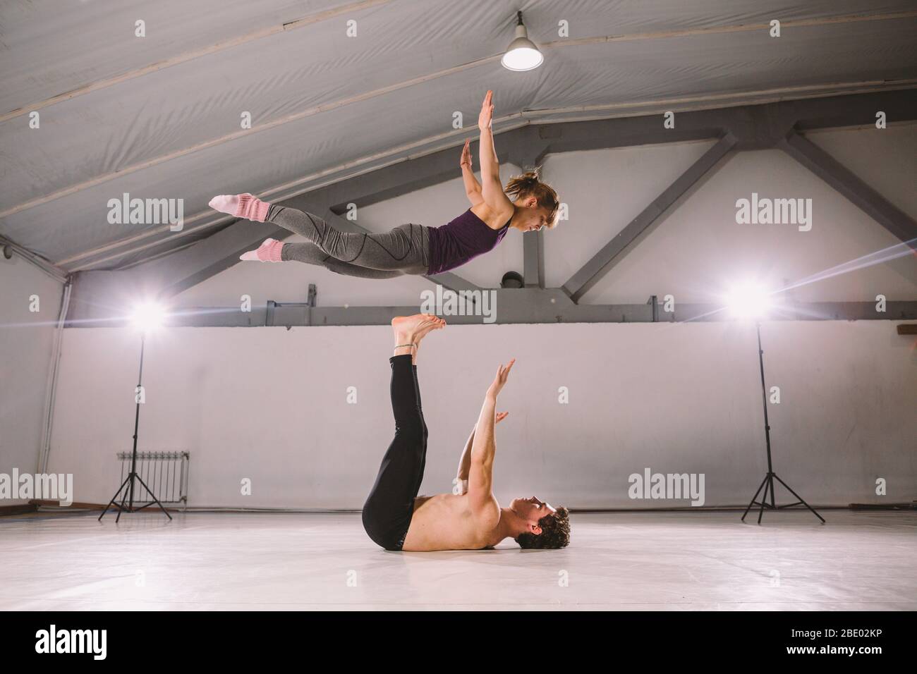 Il tema di Acroyoga e Yoga pone. Pratica di Acroyogis. Con la retroilluminazione dello studio. L'uomo base lancia il volantino donna Populs in volo. Posizione Foto Stock