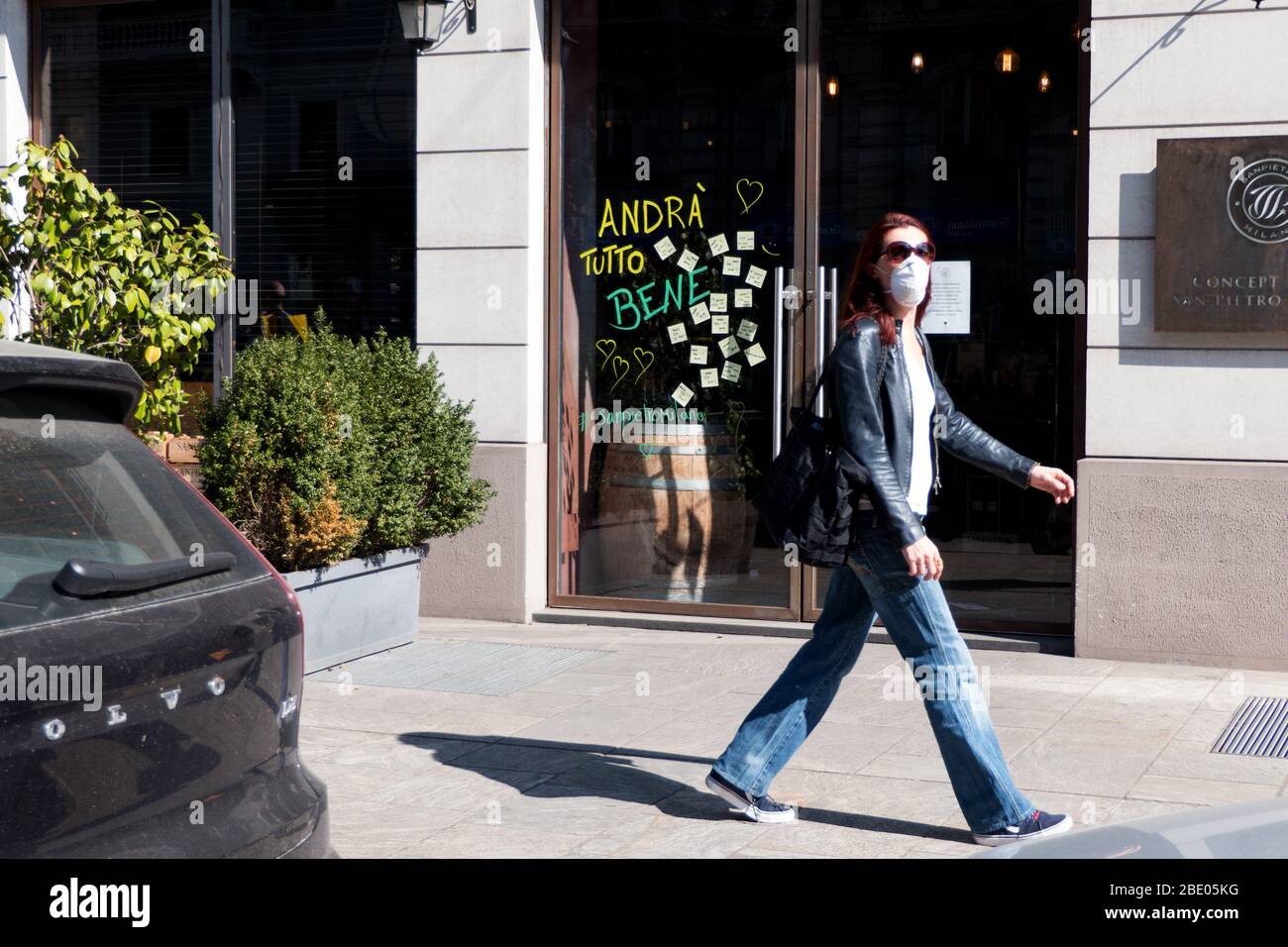 Donna con maschera protettiva e camminando per strada a Milano durante la pandemia COVID-19. Andra' tutto bene - tutto andrà bene Foto Stock