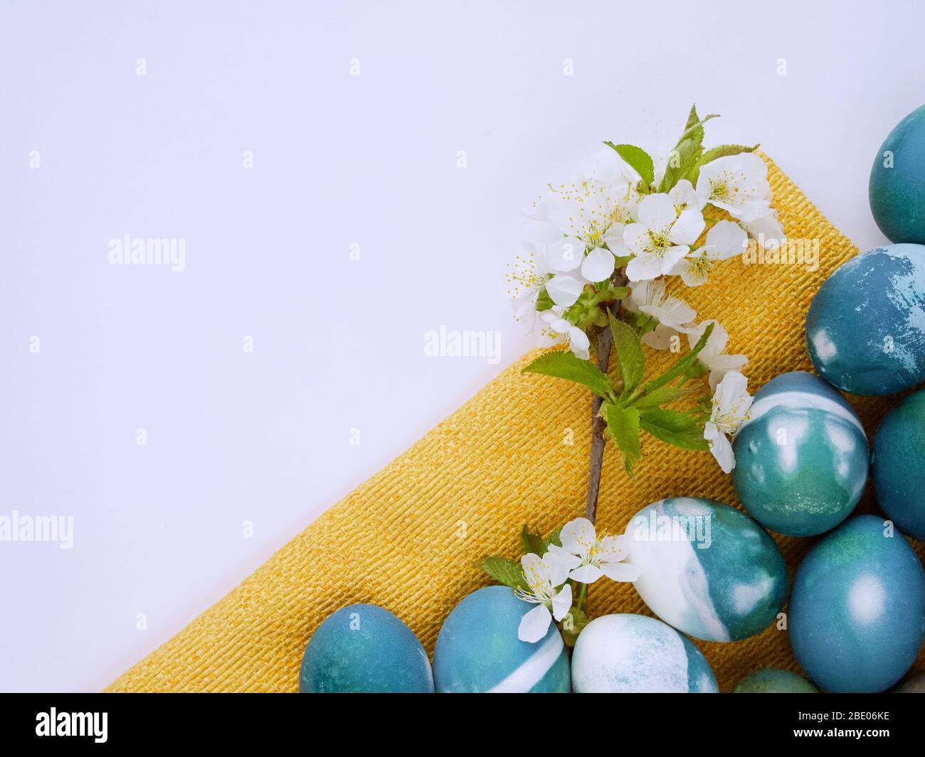 Uova di Pasqua colorate con un colore naturale di cavolo rosso su sfondo bianco e giallo con spazio vuoto decorato con fiori primaverili closeup. Foto Stock