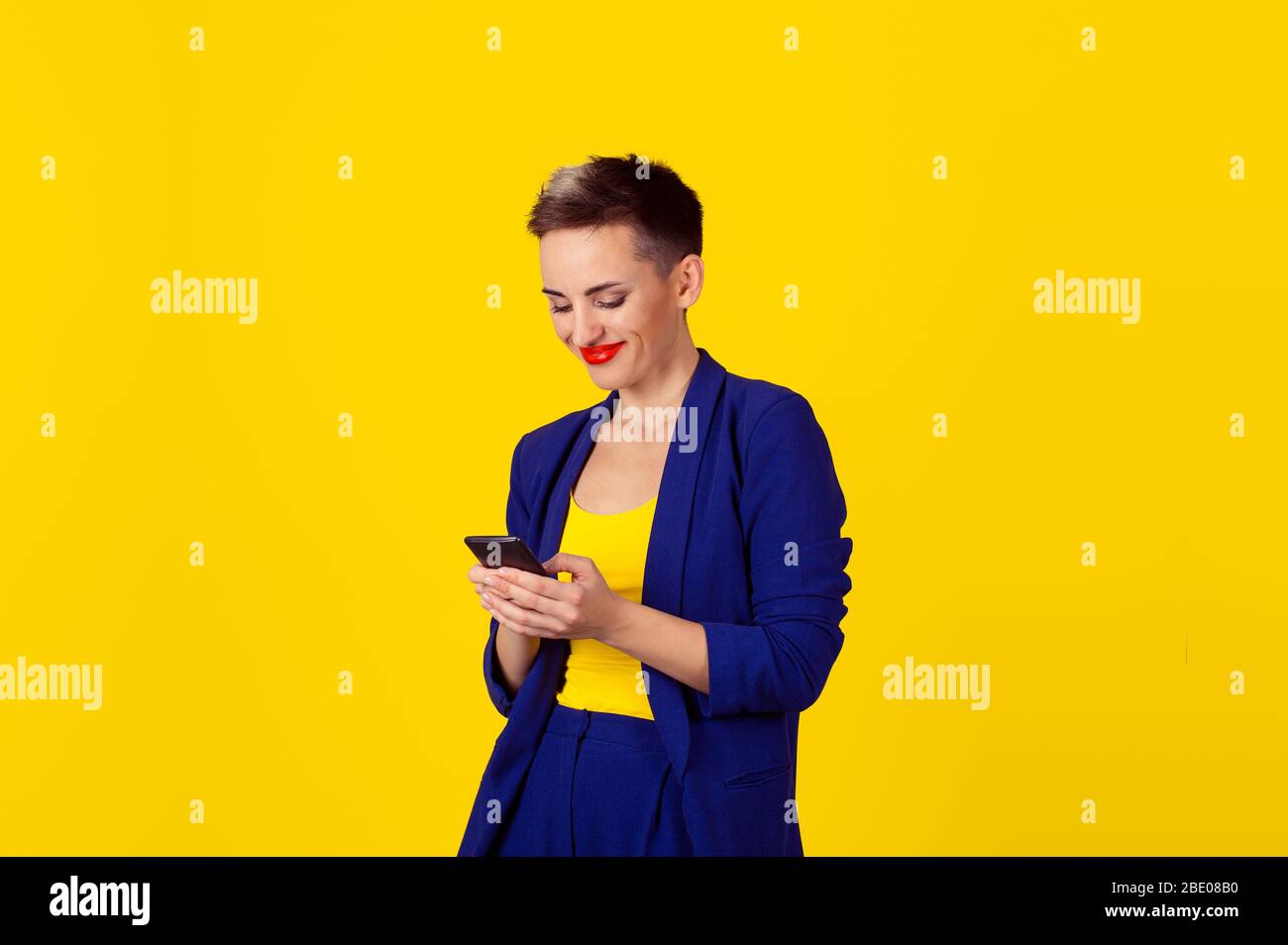 Profilo laterale ritratto closeup donna sorridente utilizzando app su uno smartphone isolato su sfondo giallo parete Foto Stock