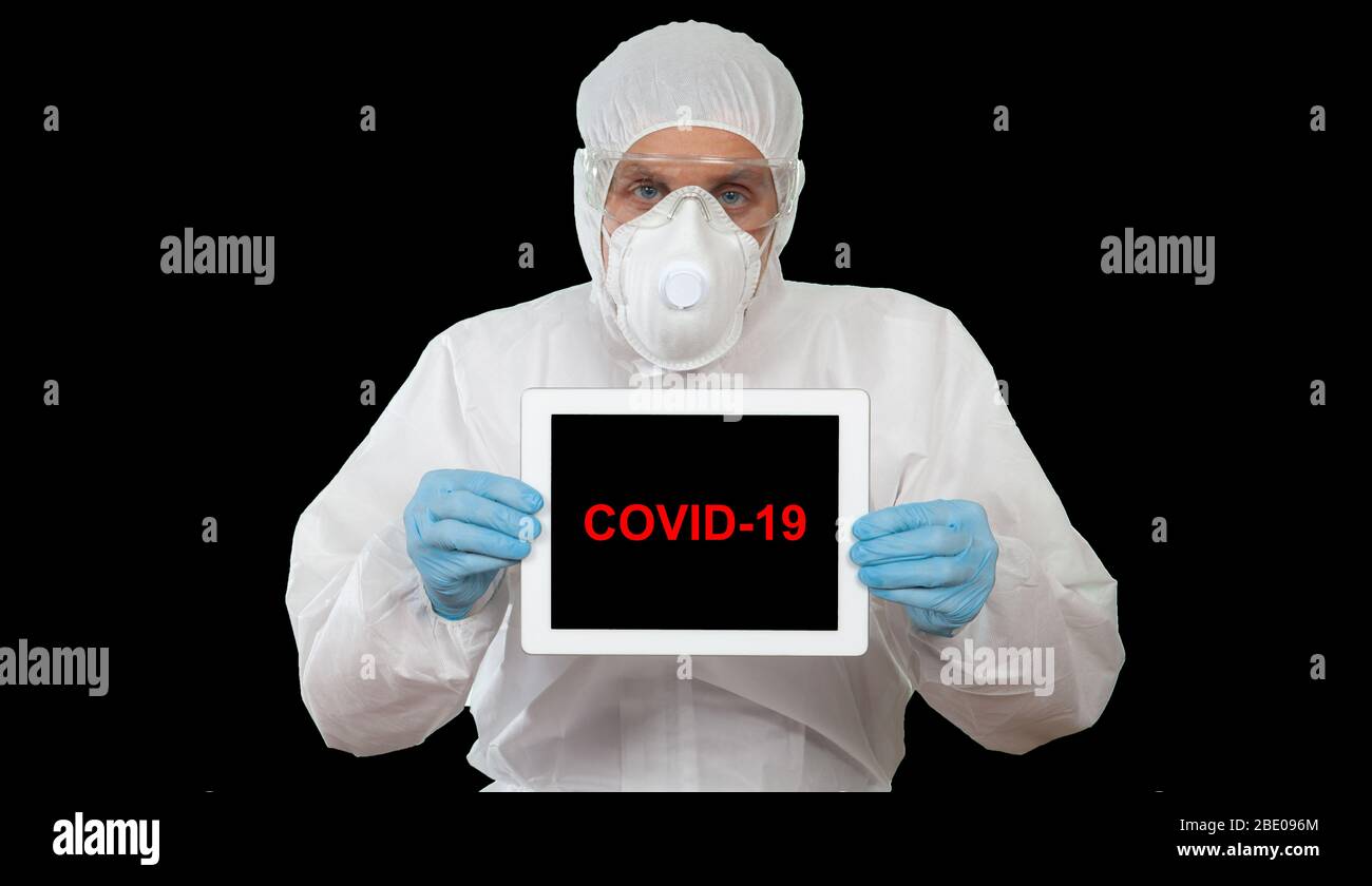 Un medico che indossa indumenti protettivi visualizza il tablet digitale con il messaggio COVID-19 Foto Stock