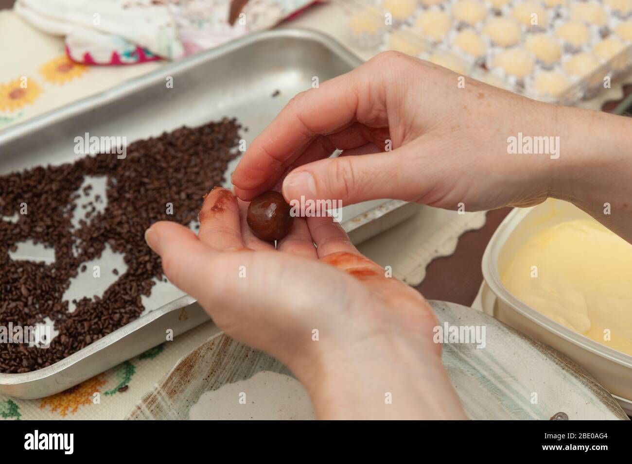 Primo piano di donne che fanno le mani deliziose e tradizionali "brigadeiros" (brasiliano Fudge Balls) sulla cima di un vassoio di alluminio. Vista dall'alto. Scatto orizzontale. Foto Stock