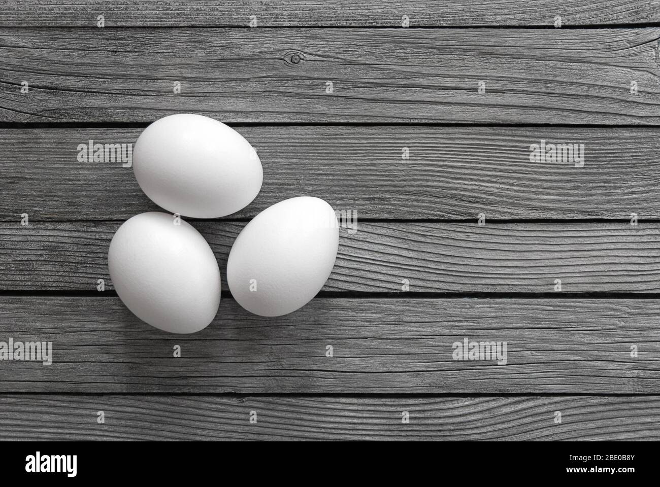 tre uova bianche su sfondo di legno grigio Foto Stock