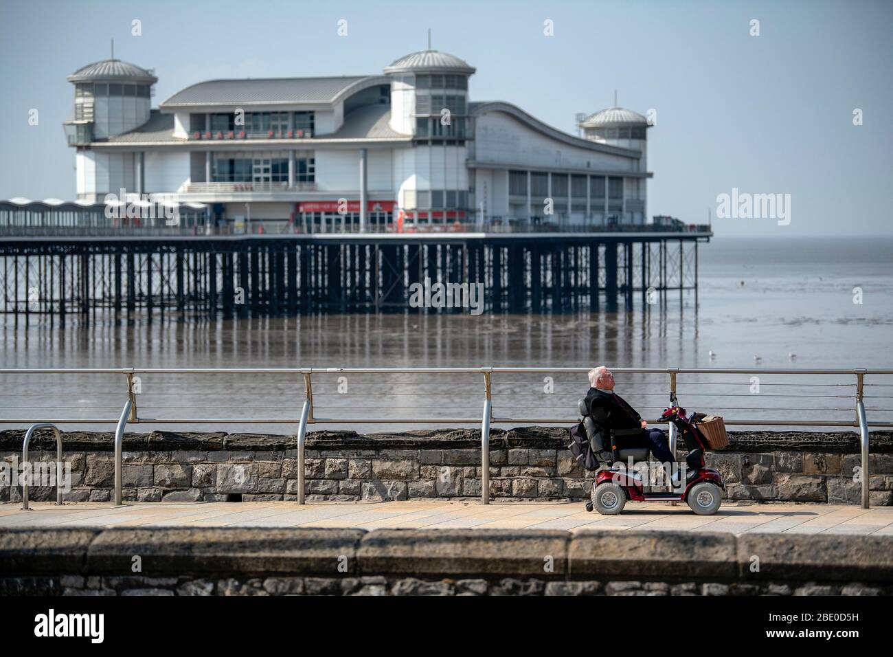 Un uomo in scooter da movimento corre lungo la Royal Parade passando davanti al Grand Pier a Weston-super-Mare durante il blocco Coronavirus nel Regno Unito. Foto Stock
