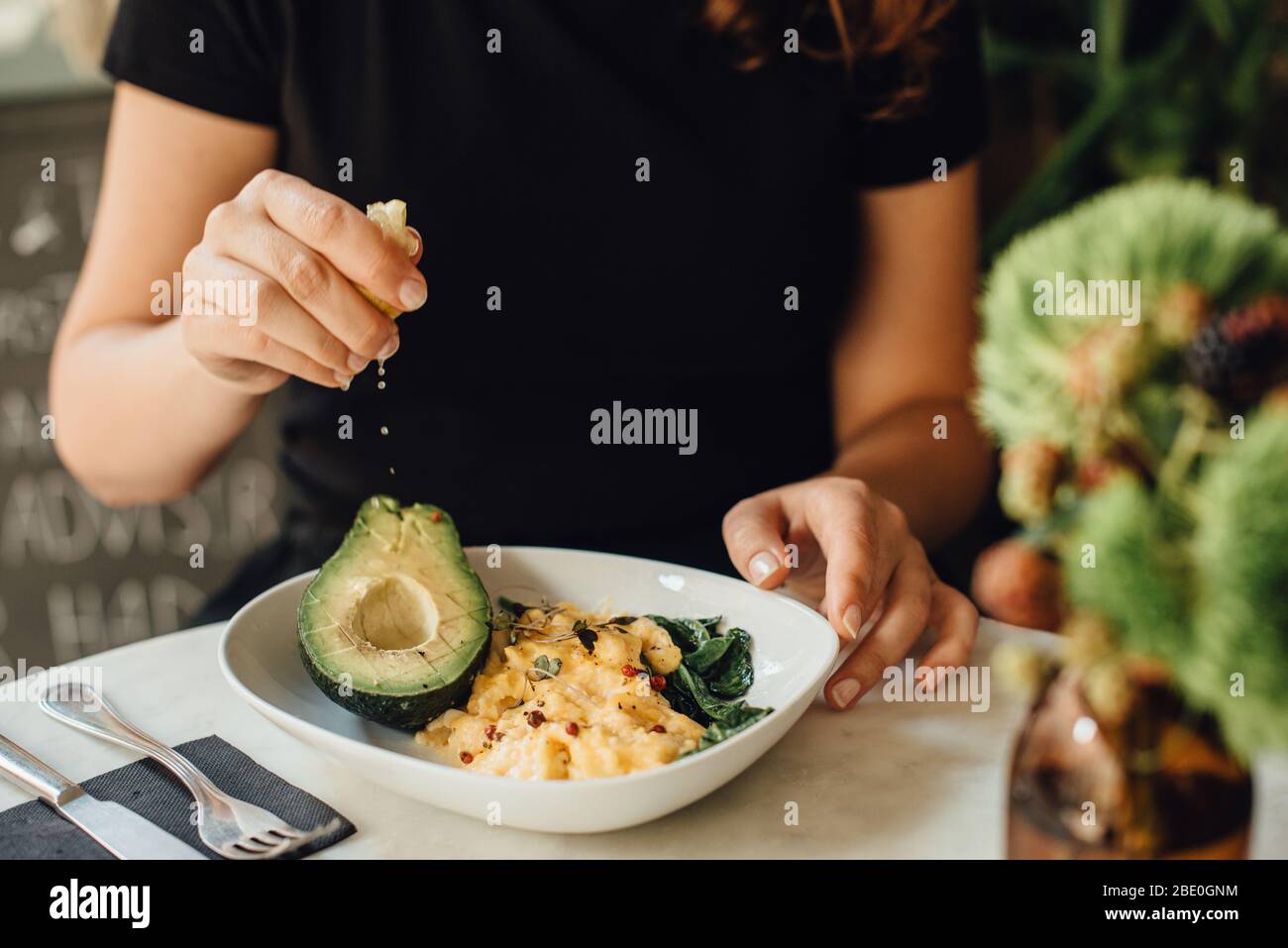 Metà della donna che mangia uova strapazzate e avocado per la colazione Foto Stock