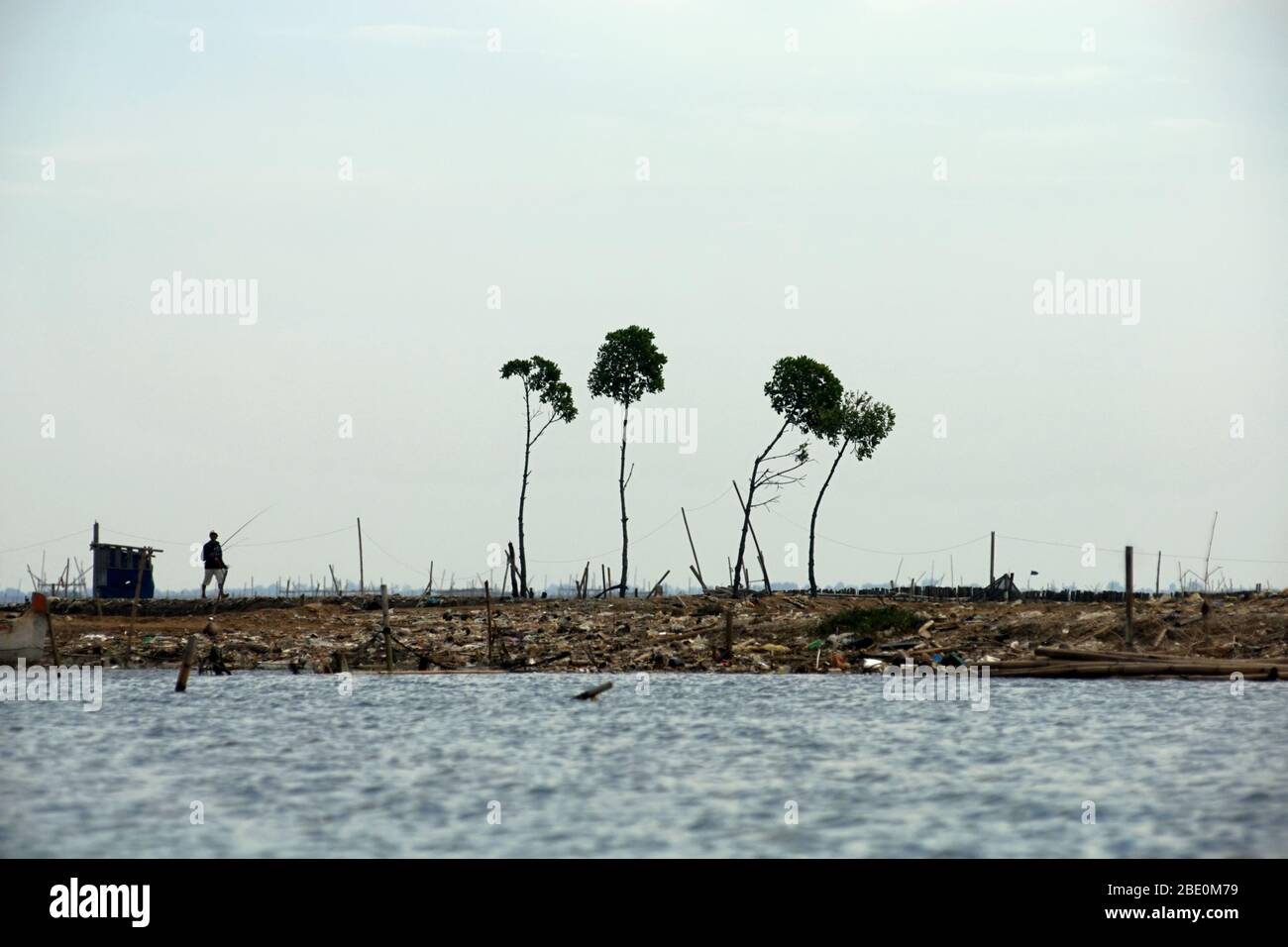 Un pescatore che cammina su una terra bonificata sull'estuario del canale delle inondazioni di Giacarta, sul confine provinciale tra Giava Occidentale e Giacarta, Indonesia. Foto Stock