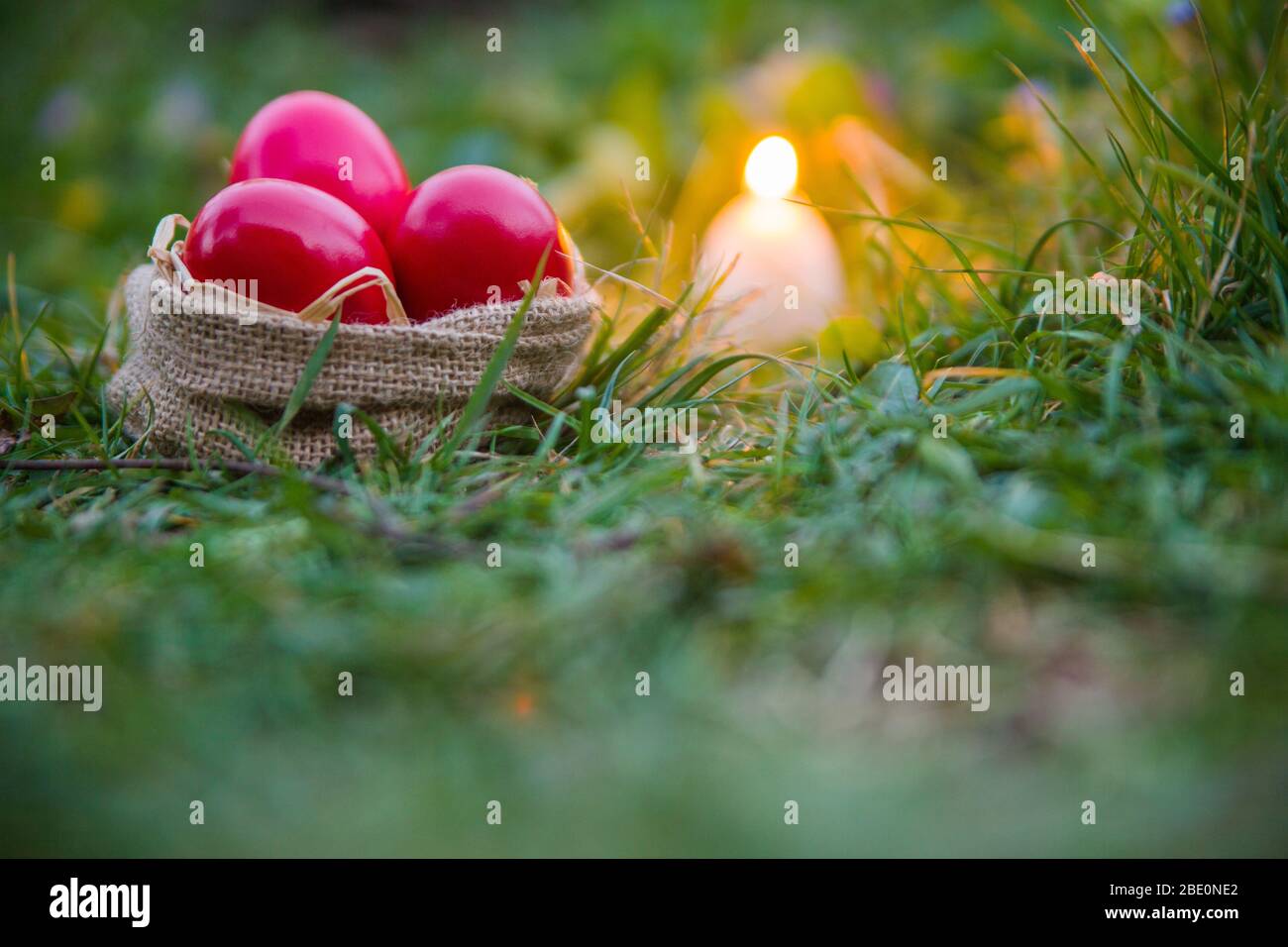 Uova rosse di Pasqua in cestino, su erba, all'aperto con candela Foto Stock