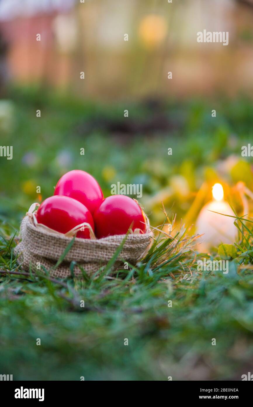 Uova rosse di Pasqua in cestino, su erba, all'aperto con candela Foto Stock