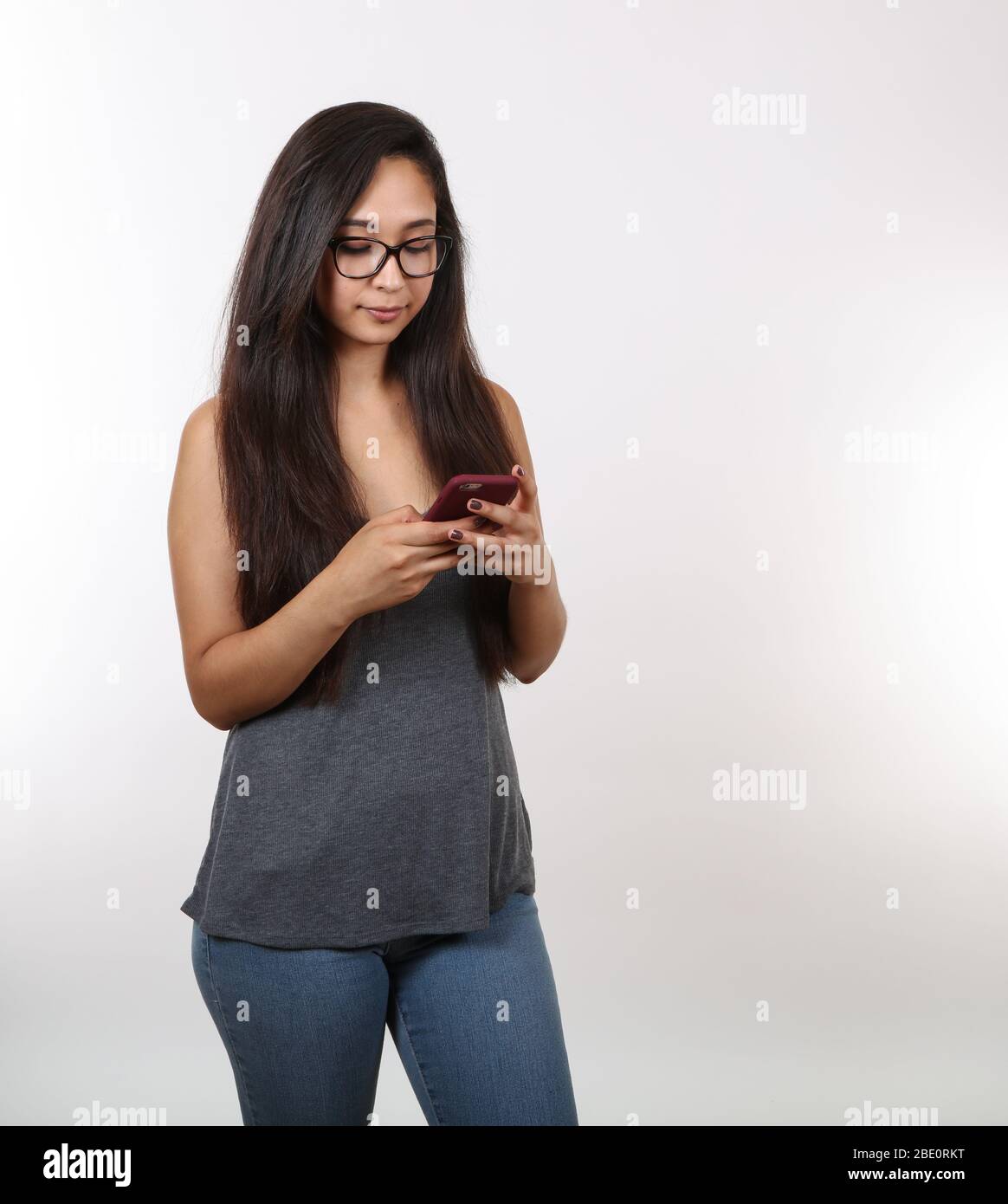 Una ragazza graziosa che indossa gli occhiali è distratta; guardando il suo telefono. Foto Stock