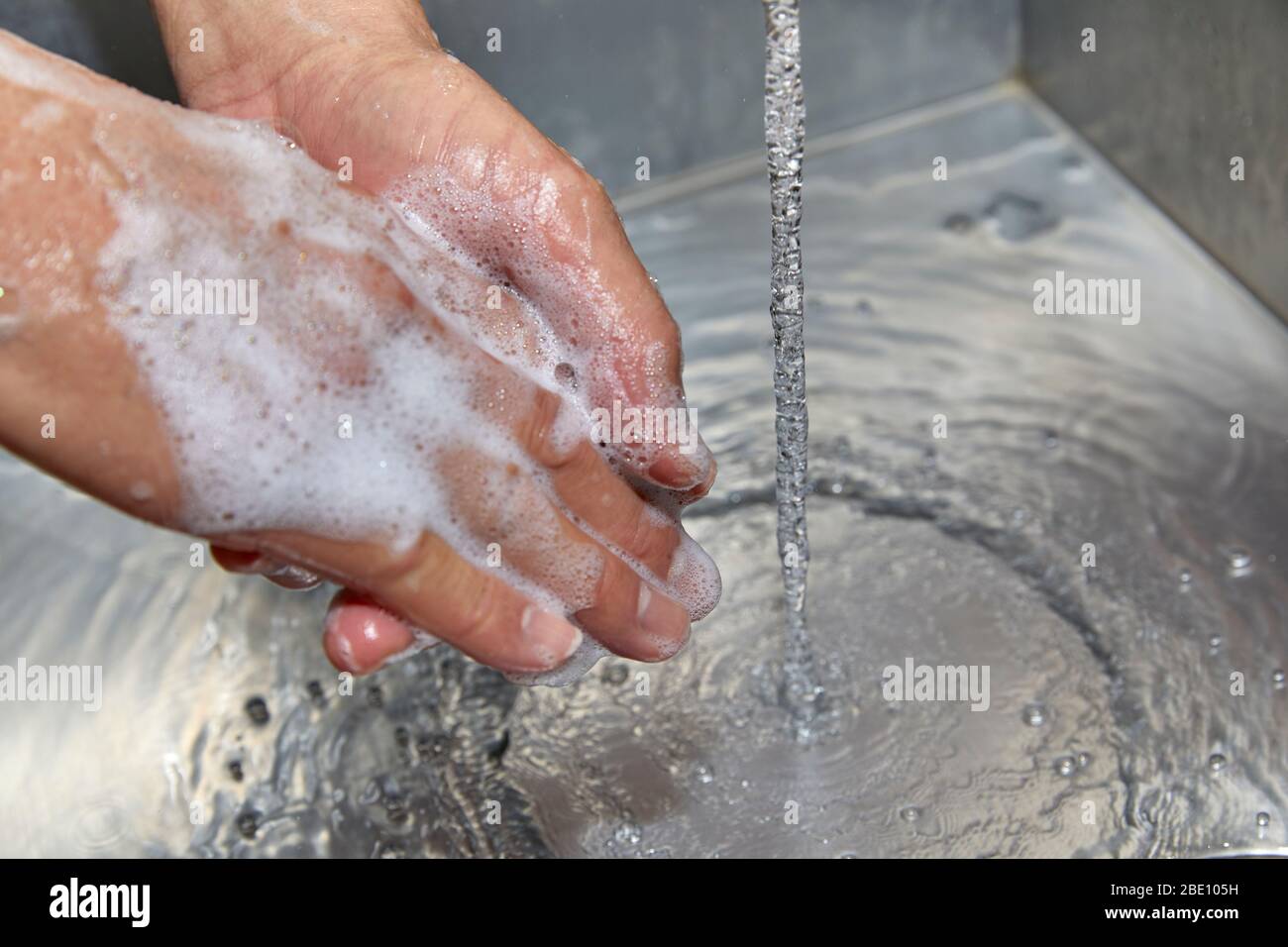 Un uomo ha le mani su un lavandino con sapone su di loro e acqua che corre mentre si lava le mani Foto Stock