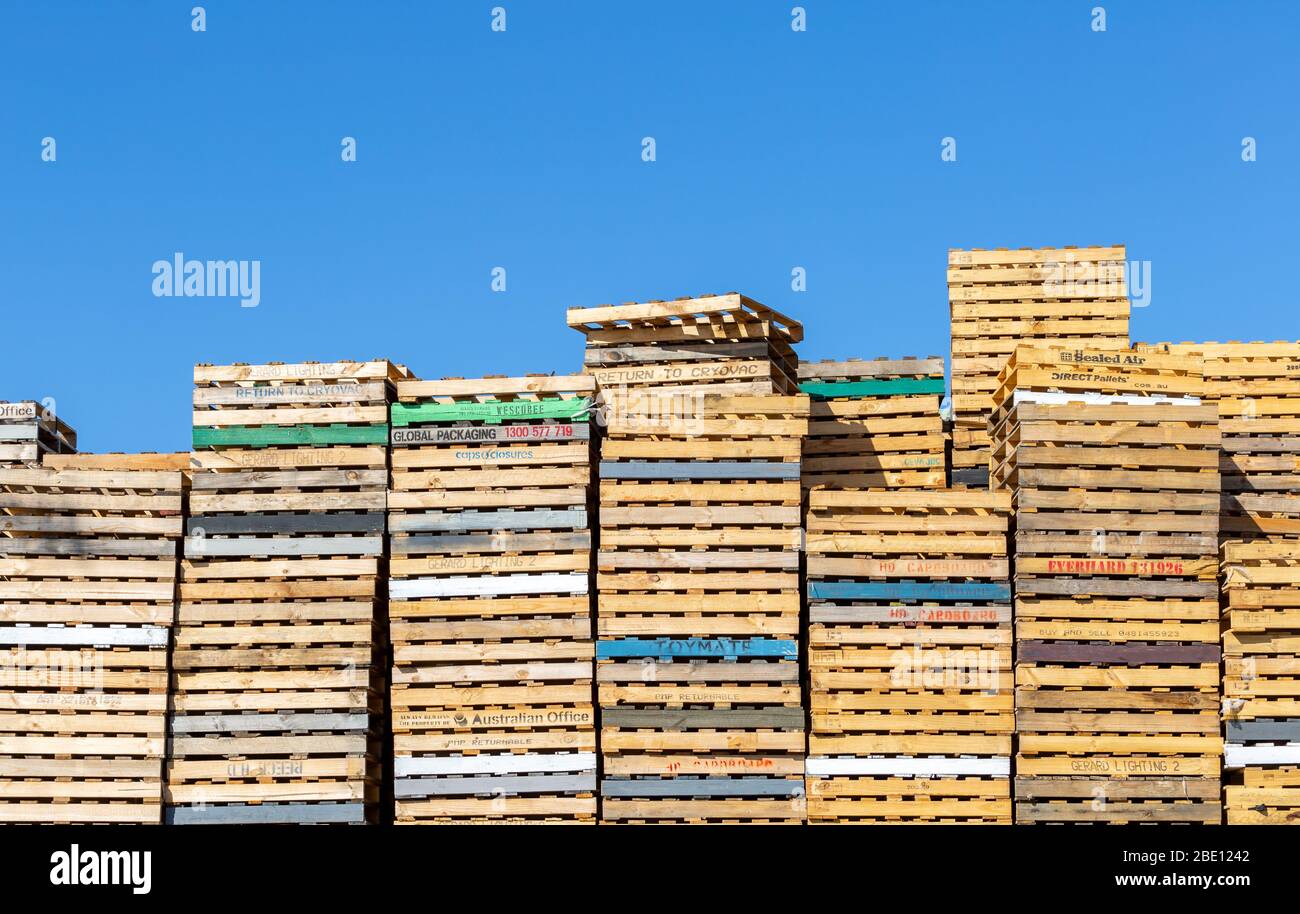 Pallet in legno impilati in un cortile industriale con sfondo blu cielo Foto Stock