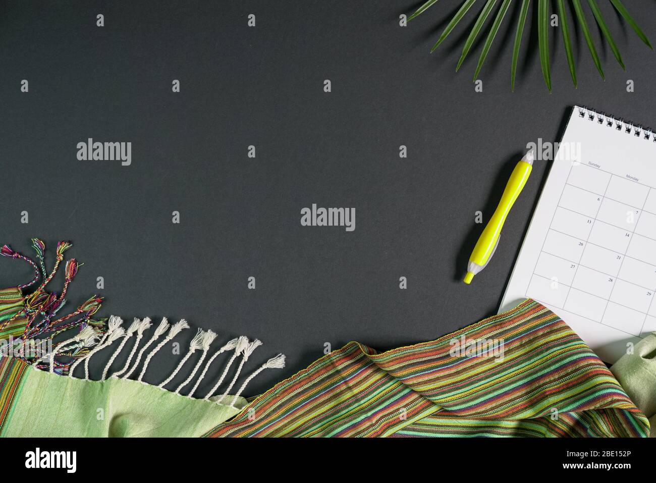 Vista dall'alto del tavolo da ufficio con pianificatore, penna, foglie di palma e tessuto imbottito. Spazio di copia. Lavorare in remoto o lavorare da casa. Foto Stock