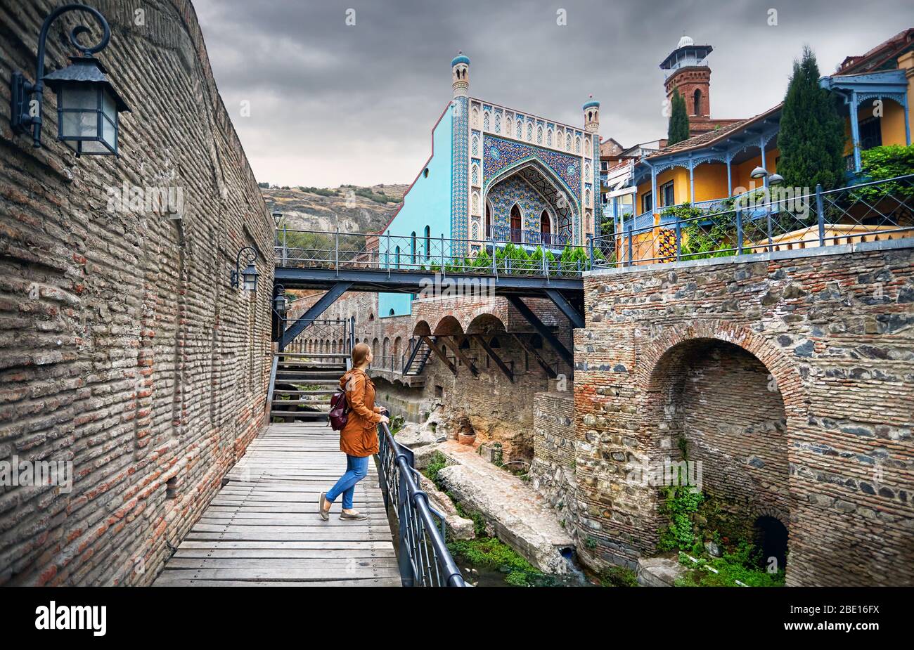Tourist donna in giacca marrone passeggiando per le vecchie strade di pubblico bagno solforico quartiere centrale di Tbilisi, Georgia Foto Stock