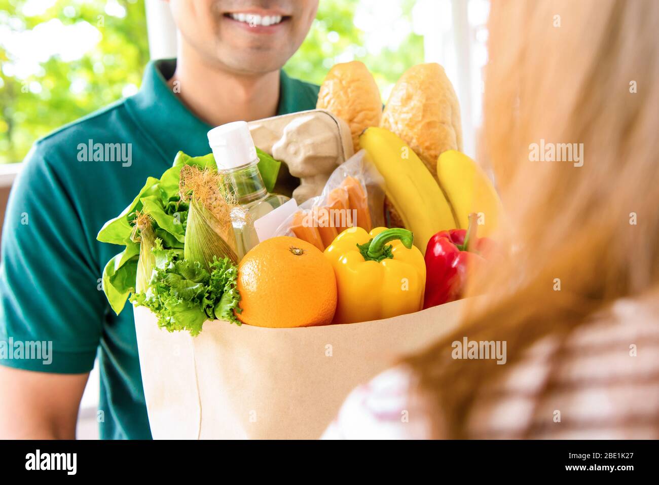 Uomo sorridente consegna che dà sacchetto della drogheria alla donna cliente a casa per il concetto di servizio di acquisto del cibo in linea Foto Stock