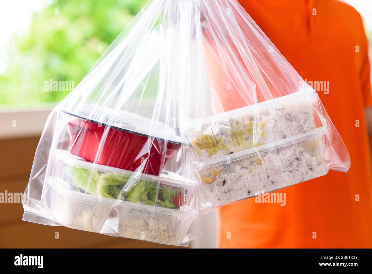 Scatole per alimenti asiatici in sacchetti di plastica consegnati al cliente a casa da uomo in uniforme arancione Foto Stock