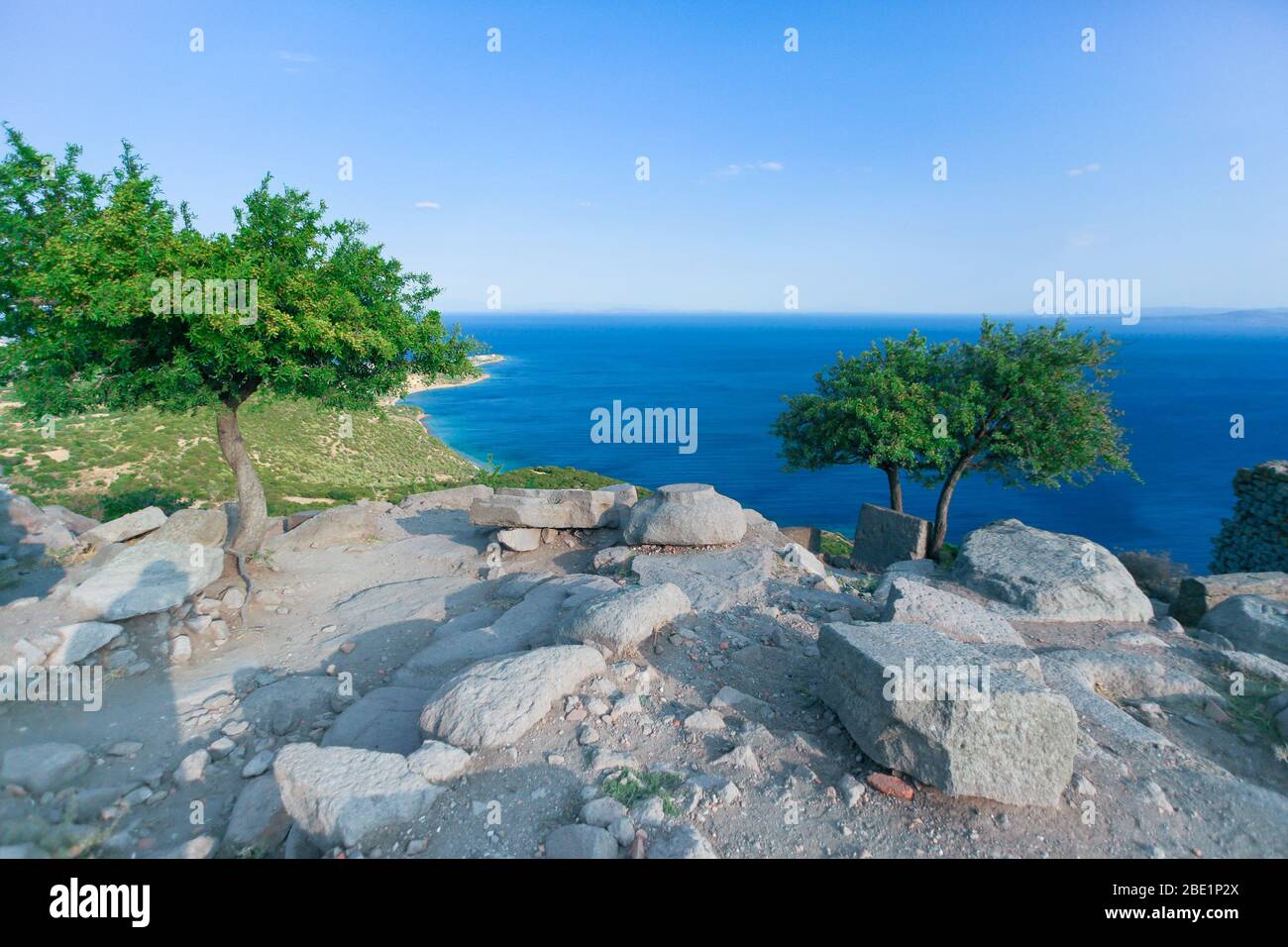 Ulivi in cima a una collina. Mar Egeo con colore blu freddo sullo sfondo. Vecchie grandi pietre antiche si siede intorno agli alberi. Foto Stock