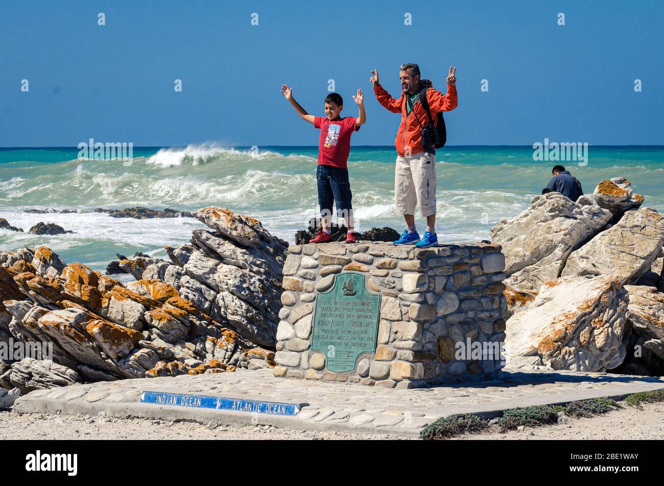 Padre e figlio in posa per una foto sul monumento in pietra nella punta più meridionale dell'Africa, dove l'Atlantico incontra l'oceano Pacifico Cape Agulhas punto Sud Africa Foto Stock