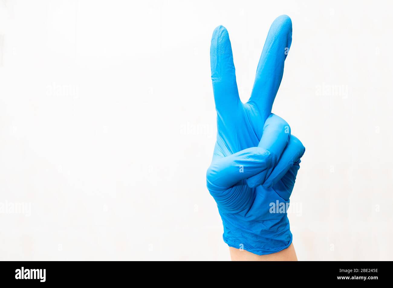 Mano sinistra di un medico con guanto che fa segno di vittoria. Concetto di guarigione. Foto Stock