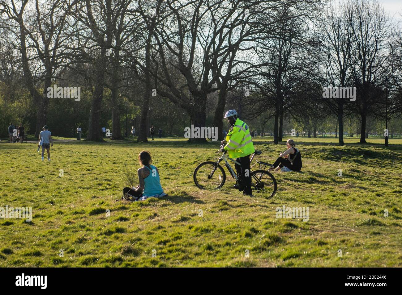 Un poliziotto in bicicletta chiede a una ragazza di muoversi per violare le regole di blocco su Clapham Common a Londra per ridurre la diffusione Coronavirus Covid-19 Foto Stock