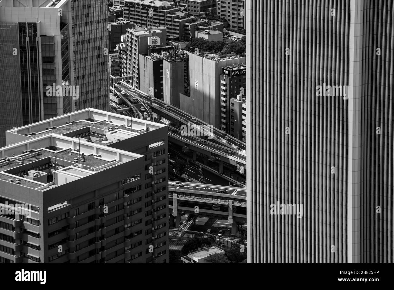 Un viadotto ferroviario elevato si snoda tra edifici di uffici, le lettere illuminate "APA Hotel" sono visibili su uno di essi, fotografate da The Okura Tokyo, quartiere di Minato, Giappone. Foto Stock