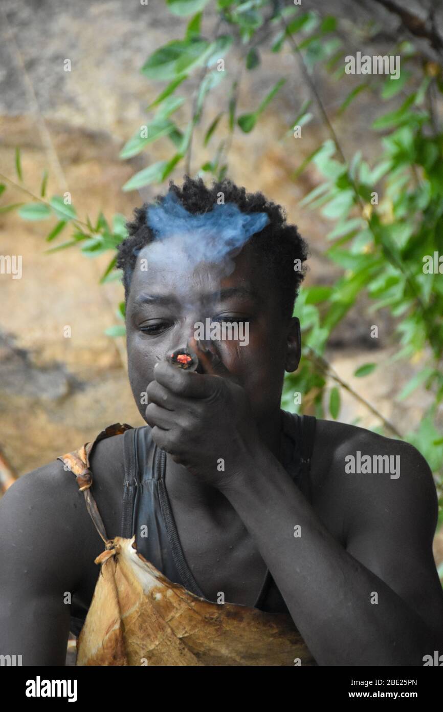 Hadzabe uomo fumo da un tradizionale tubo di argilla fotografato vicino al lago Eyasi, Tanzania Africa Foto Stock