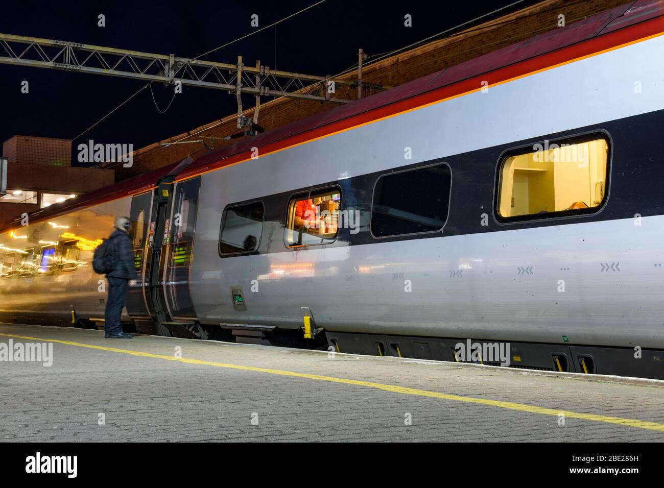 Scena notturna di un passeggero che aspetta le porte per aprire su un treno Virgin Pendolino alla stazione ferroviaria di Coventry Foto Stock