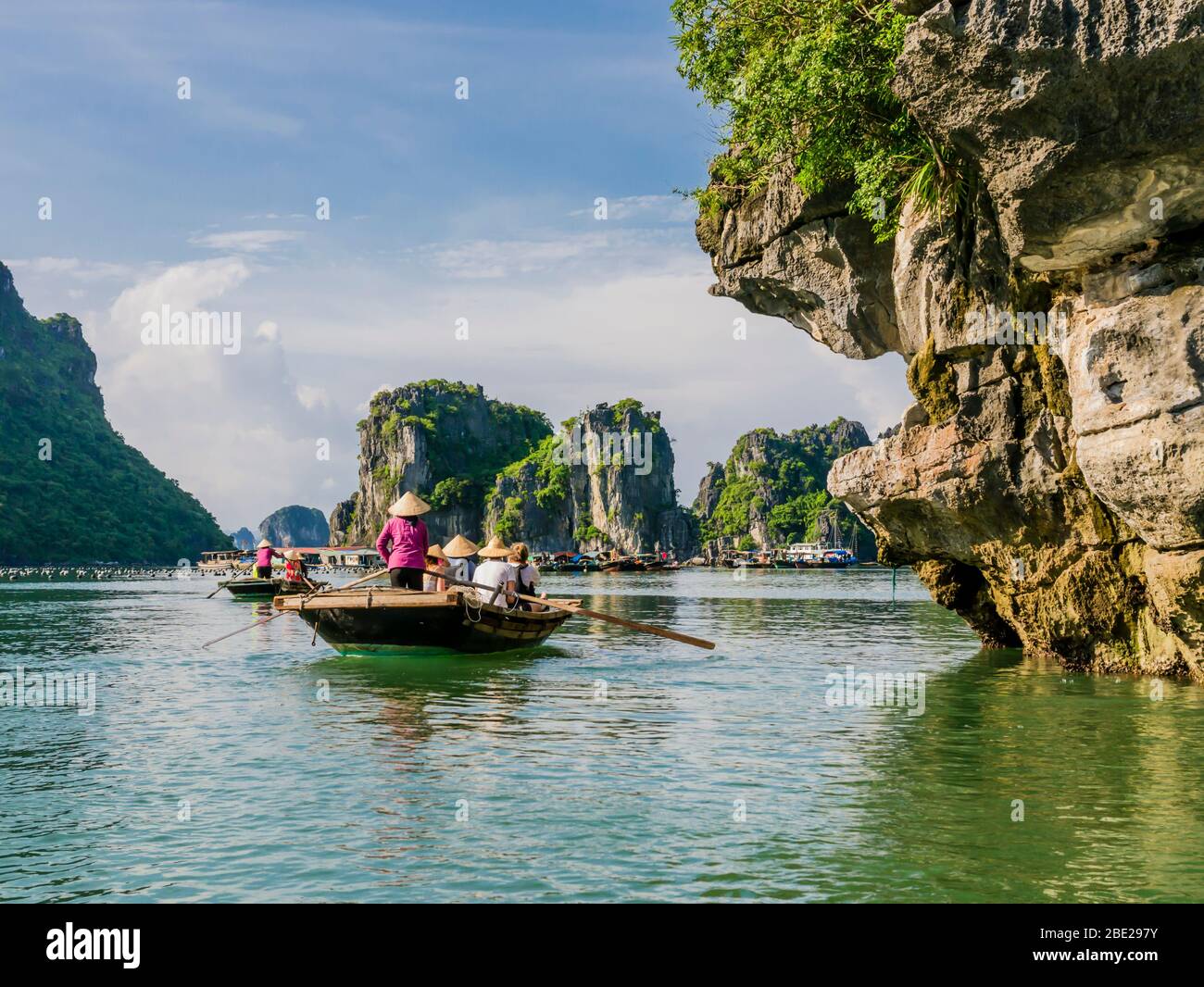 I turisti che si godono una gita in barca con guide locali attraverso le maestose montagne calcaree della baia di ha Along, Vietnam Foto Stock