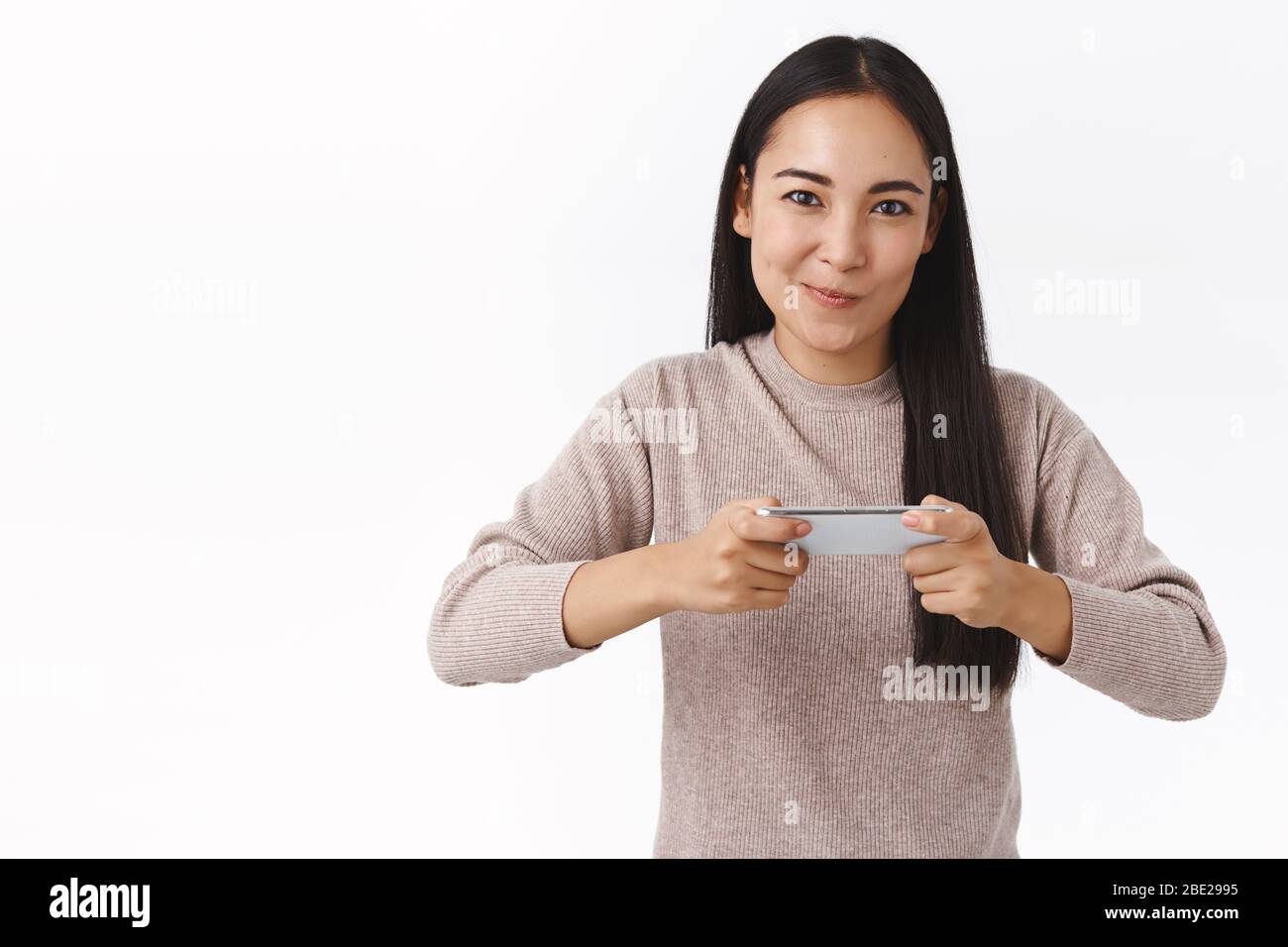 Sassy e entusiasta e sorridente allegra donna asiatica, amici pronti battere segnare in gioco, tenendo smartphone orizzontalmente, grinning eccitato Foto Stock