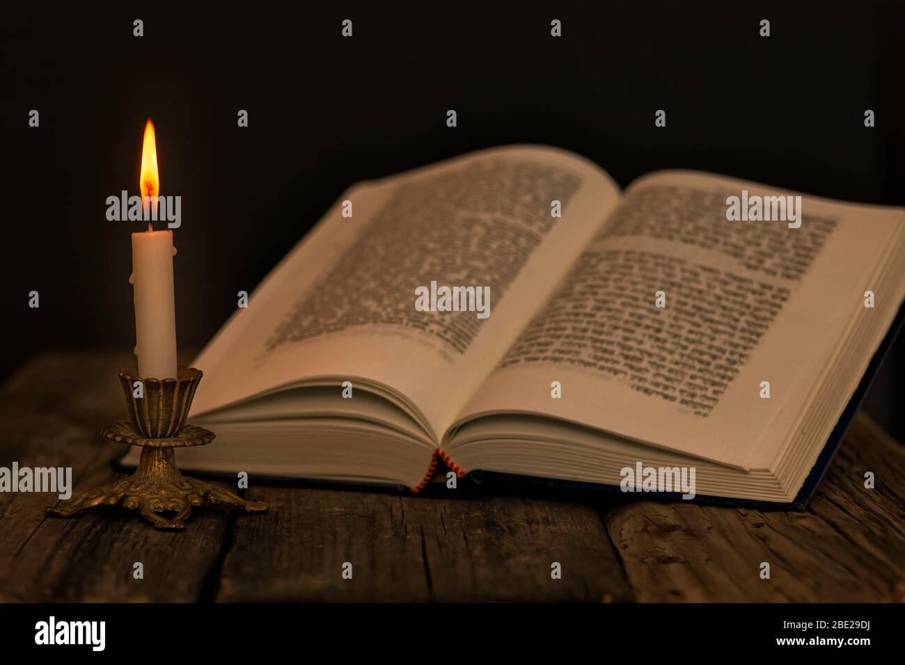 Apri Torah e una candela bruciante in un candeliere su una superficie di legno su uno sfondo scuro da vicino Foto Stock