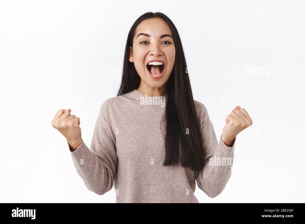 Emozionata e felice ragazza asiatica clench pugni in potente moto trionfante, pompa pugno e gridare sì da stupore e gioia, sorridendo compiaciuto Foto Stock