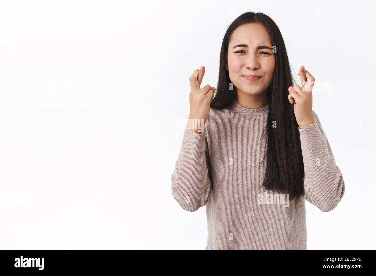 Ragazza ha messo tutto lo sforzo che prega, desidera sogno venire allineare. Donna asiatica carina e allarmata in maglione d'inverno, barrette incrociate per la buona fortuna, squinting e. Foto Stock