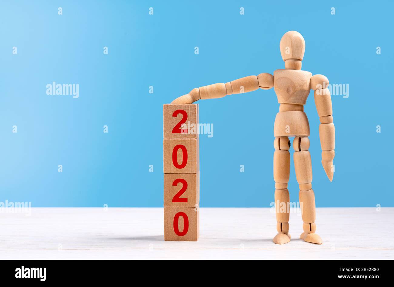 Figura di manichino in legno alzate una mano e indossate una torre di cubi con iscrizione rossa 2020 anni. Si trova in studio su sfondo blu. Concetto di w Foto Stock