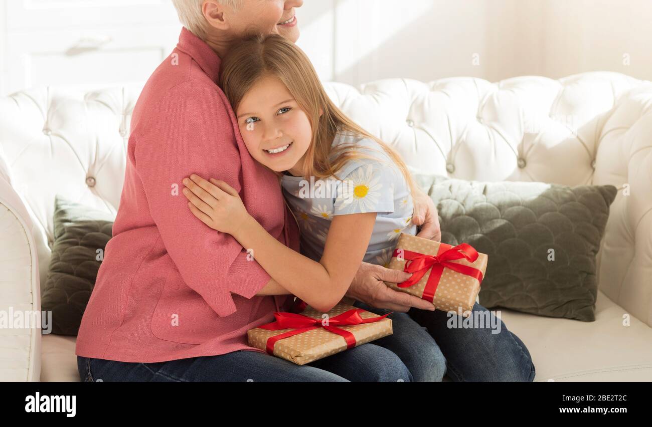 Ragazza sorridente e la sua nonna con regali che abbracciano in stanza luce, spazio vuoto Foto Stock