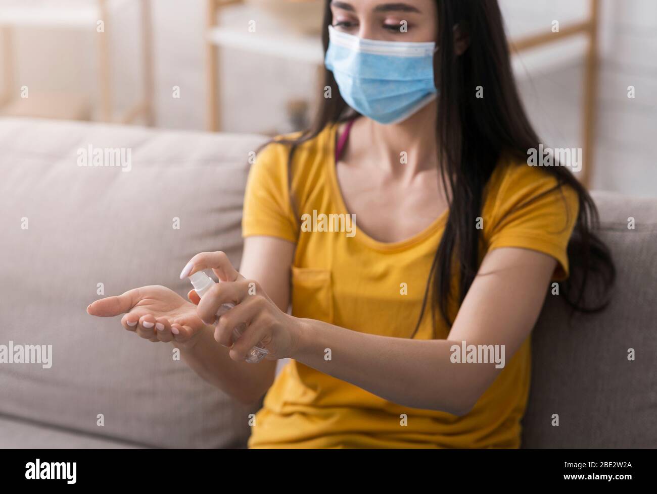 Igiene durante l'epidemia di coronavirus. Ragazza millenaria in maschera monouso applicando antisettico sulle mani a casa Foto Stock
