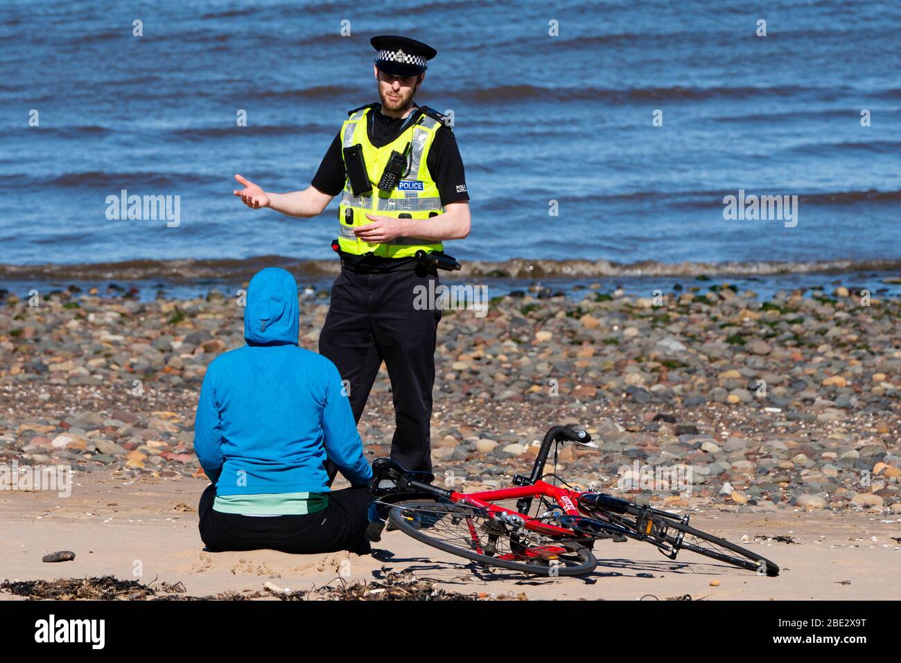 Portobello, Edimburgo. Scozia, Regno Unito. 11 aprile 2020. Pasqua weekend di festa in banca Sabato pomeriggio in tempo molto caldo soleggiato il pubblico è all'aperto, allenandosi e camminando sulla spiaggia di Portobello. La spiaggia e il lungomare erano molto tranquilli e la gente si stava esercitando per lo più a distanza sociale. Nella foto: La polizia che pattina la passeggiata si ferma per parlare con una donna sulla spiaggia. Le è stato chiesto di andare avanti. Iain Masterton/Alamy Live News Foto Stock