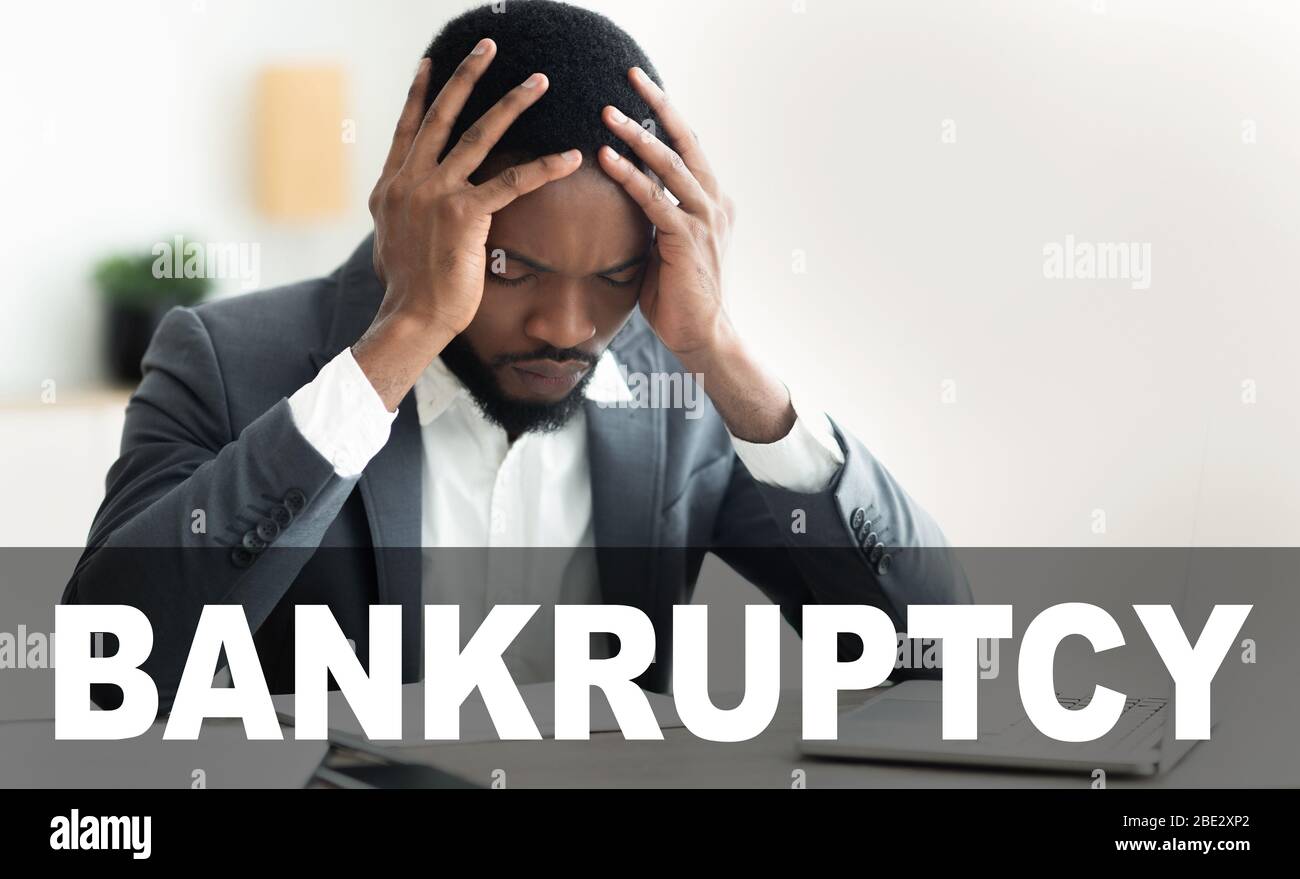 COVID-19 ha provocato una crisi finanziaria. Un uomo d’affari africano-americano che stringeva la testa nella disperazione in ufficio Foto Stock