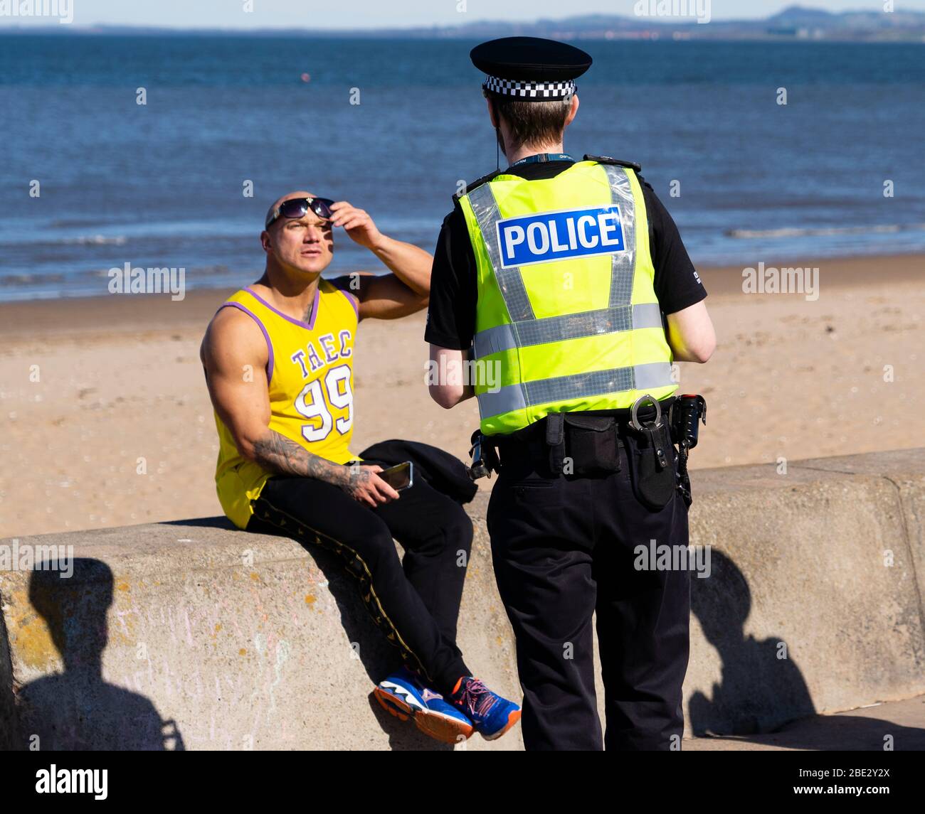 Portobello, Edimburgo. Scozia, Regno Unito. 11 aprile 2020. Pasqua weekend di festa in banca Sabato pomeriggio in tempo molto caldo soleggiato il pubblico è all'aperto, allenandosi e camminando sulla spiaggia di Portobello. La spiaggia e il lungomare erano molto tranquilli e la gente si stava esercitando per lo più a distanza sociale. Nella foto: La polizia che pattina la passeggiata si ferma per parlare con un uomo seduto sul muro di mare. Gli fu chiesto di andare avanti. Iain Masterton/Alamy Live News Foto Stock