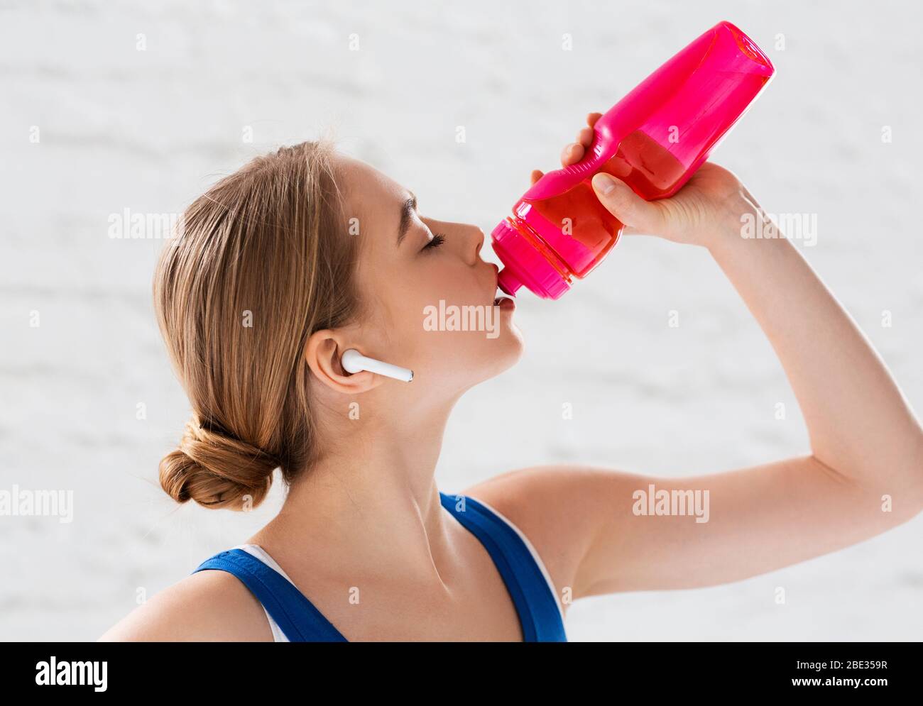 Idratazione durante l'allenamento. Atleta millenario che beve acqua da una bottiglia sportiva in interni Foto Stock