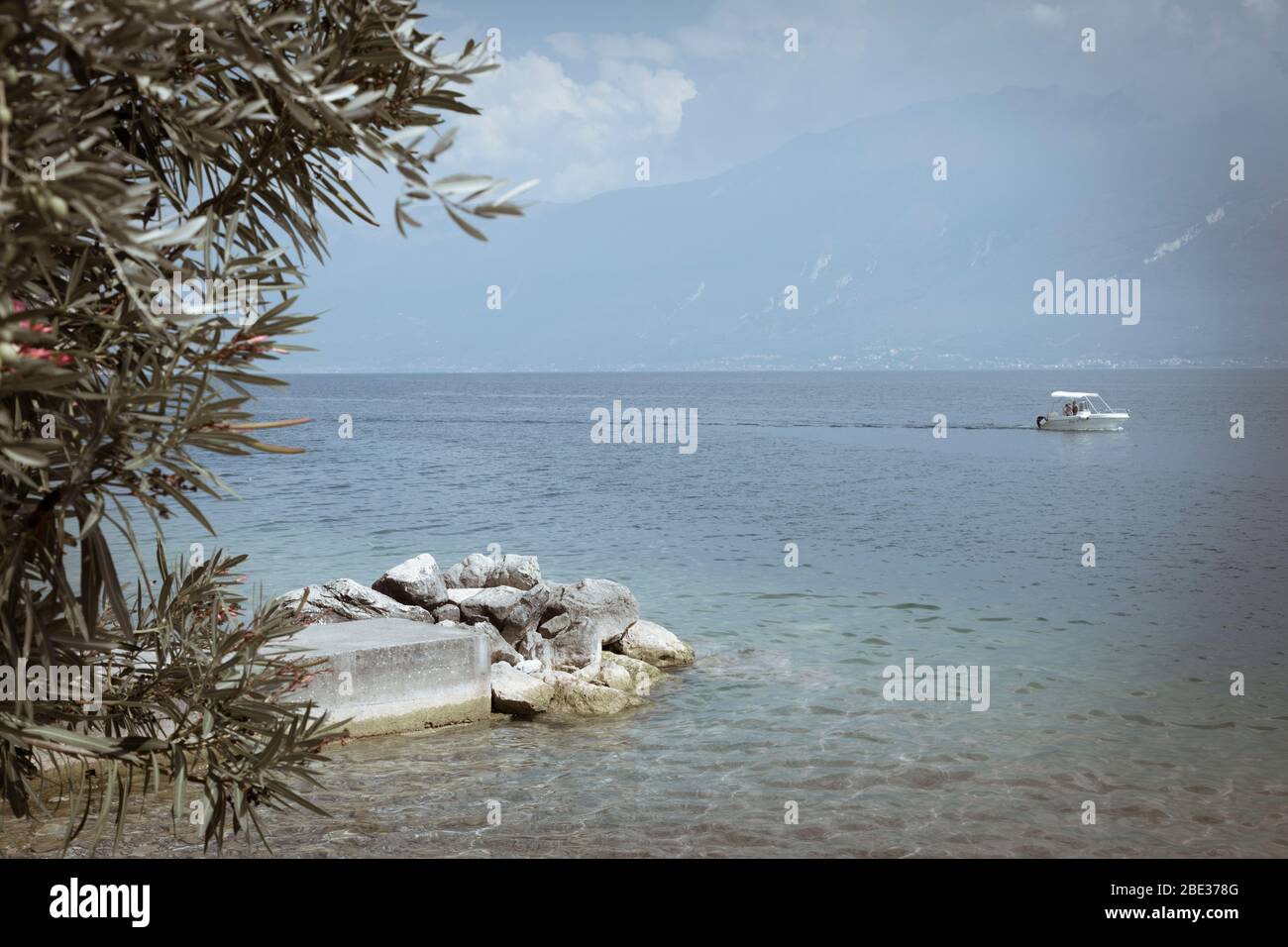 Una piccola barca da diporto con ombrellone attraversa lentamente il Lago di Garda. Foto Stock